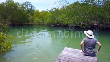 亚洲女孩戴帽子的视频坐在<strong>潮间带</strong>森林旁边的一个小码头上